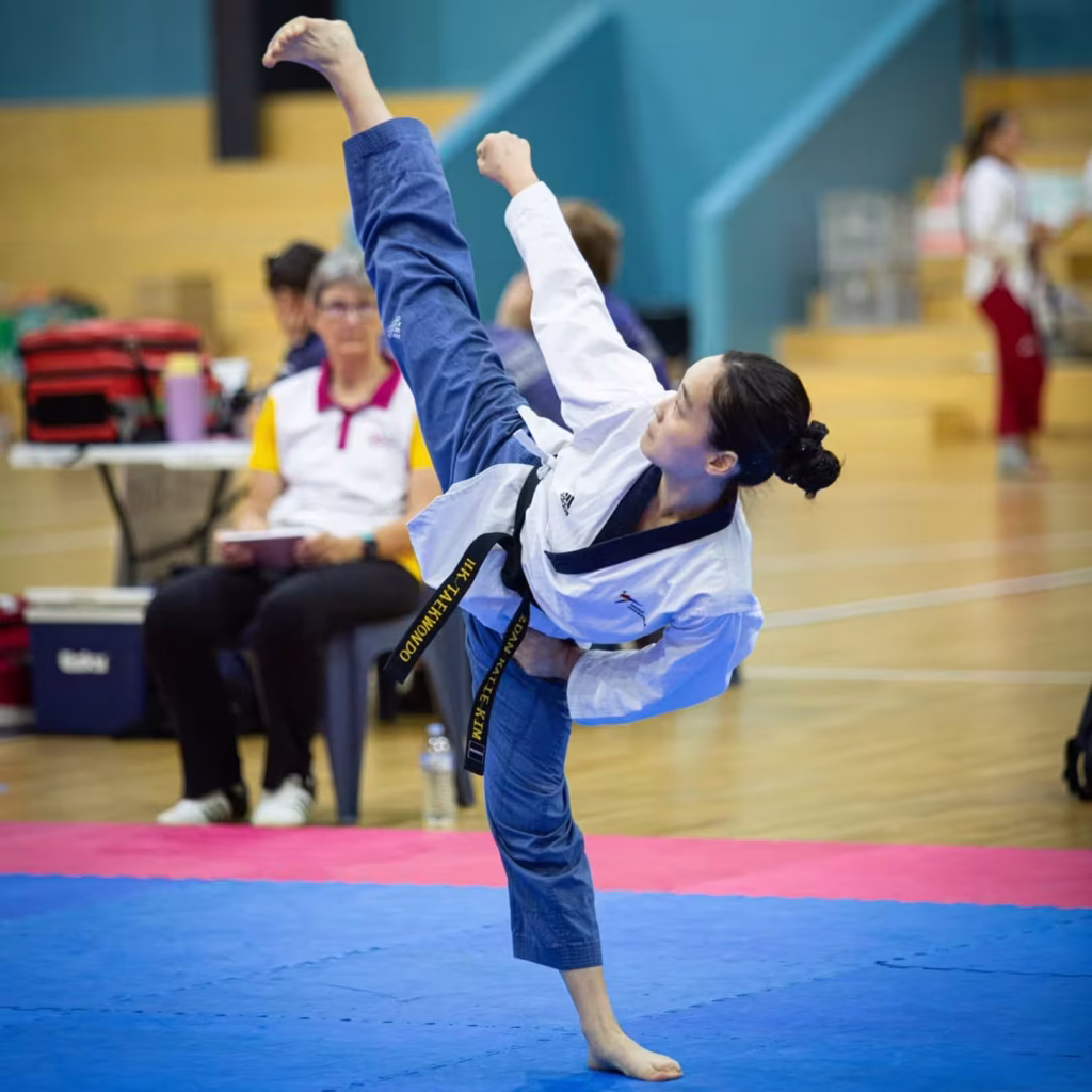 Black belt instructor from taekwondo classes Brisbane executing a high kick during a competition